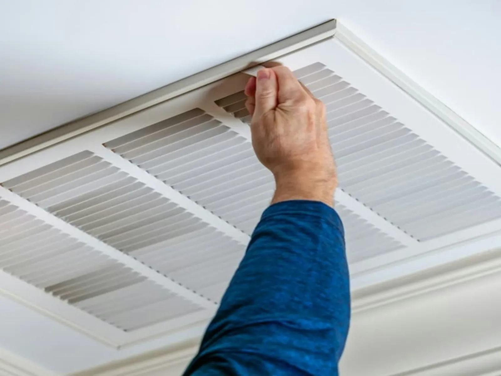 Hands opening a ceiling air-conditioning return grille to access the filter