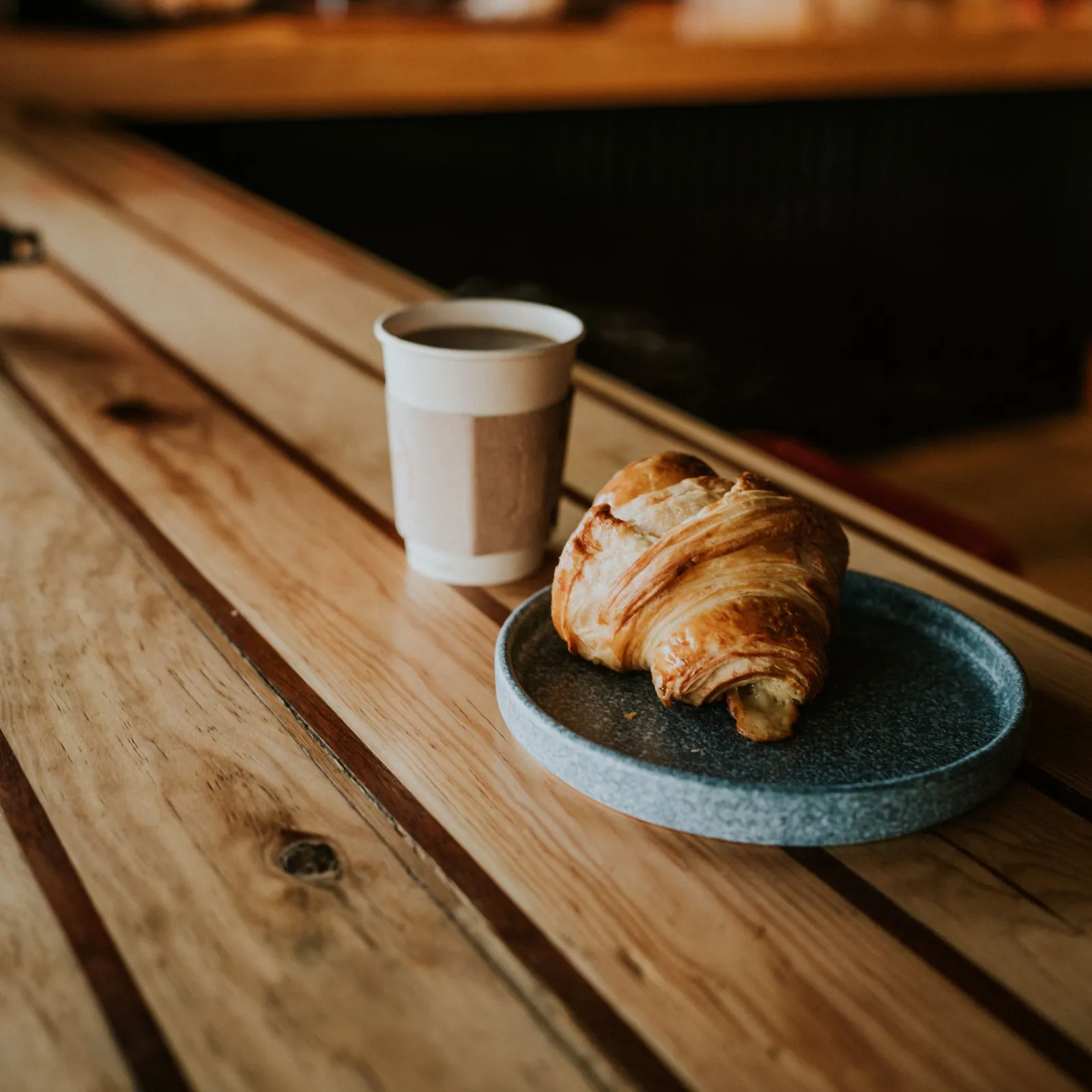 Butter croissant on a stone plate beside a paper coffee cup on a cafe counter
