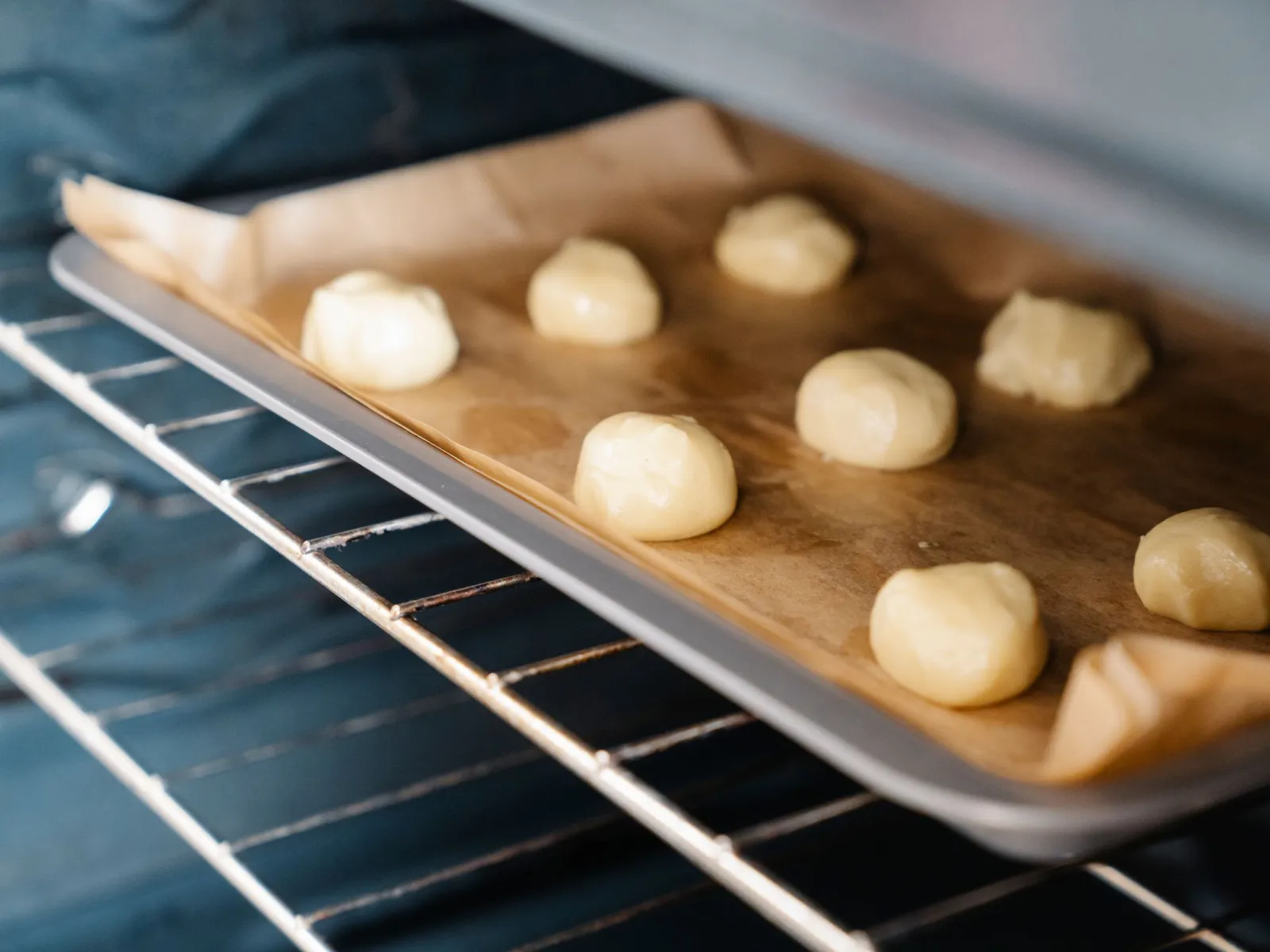 Rows of raw dough balls on a parchment-lined tray sliding into the oven