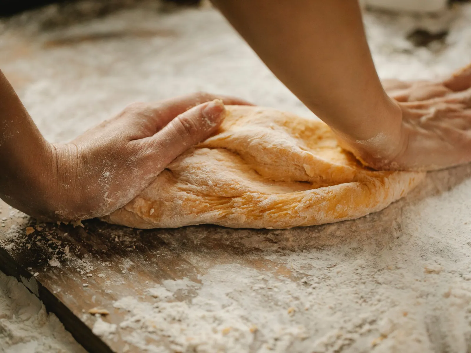Hands pressing golden dough onto a flour-dusted wooden board