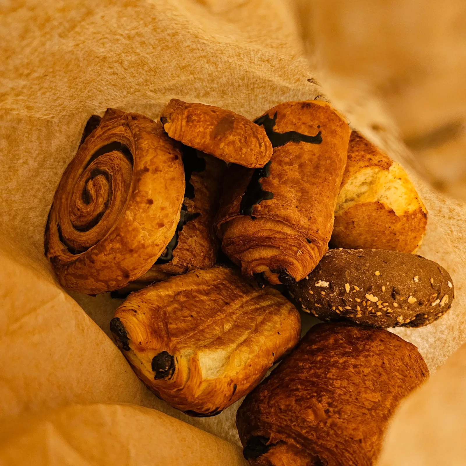 Pains au chocolat and seeded rolls tucked into a paper bakery bag