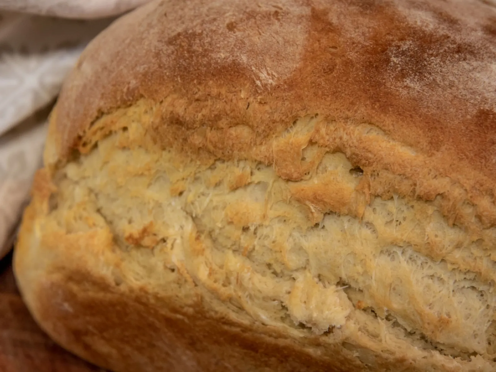 Close-up of a rustic loaf's golden crust beside a patterned linen cloth