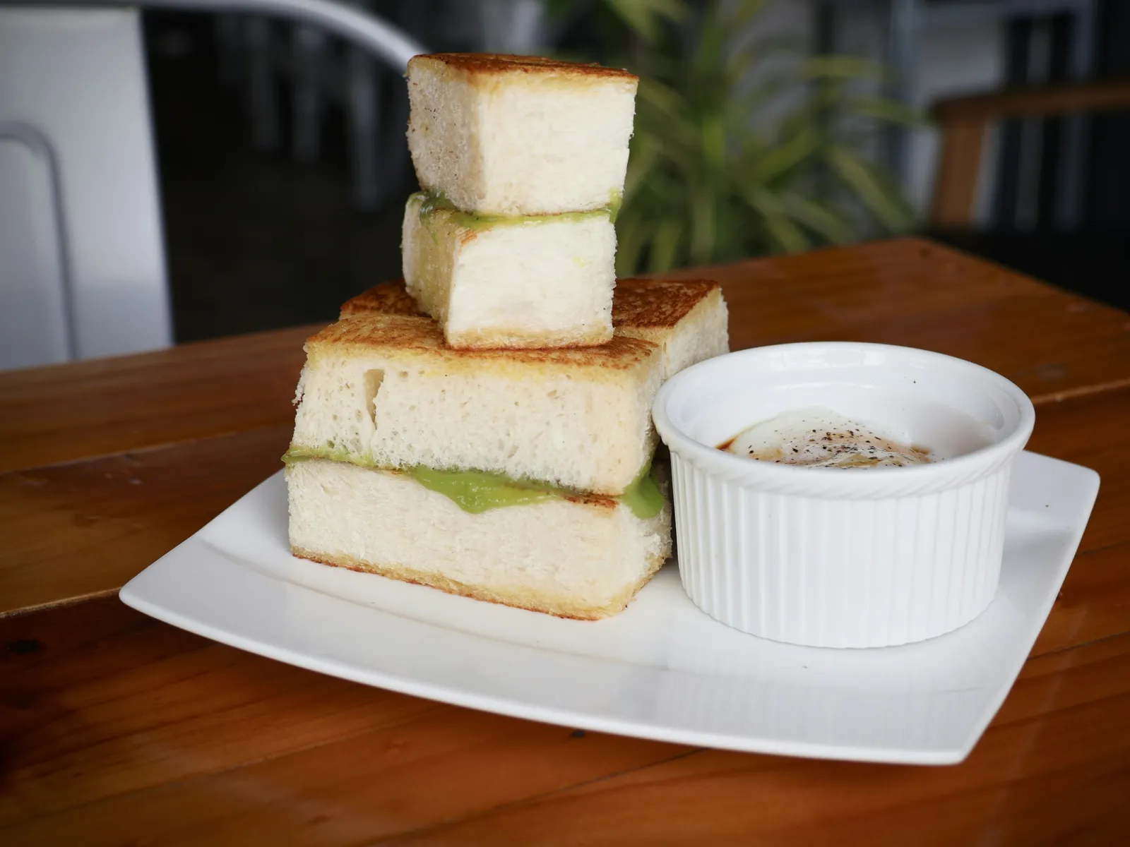 Stacked kaya toast with pandan spread and soft-boiled eggs in a ramekin on a wooden kopitiam table