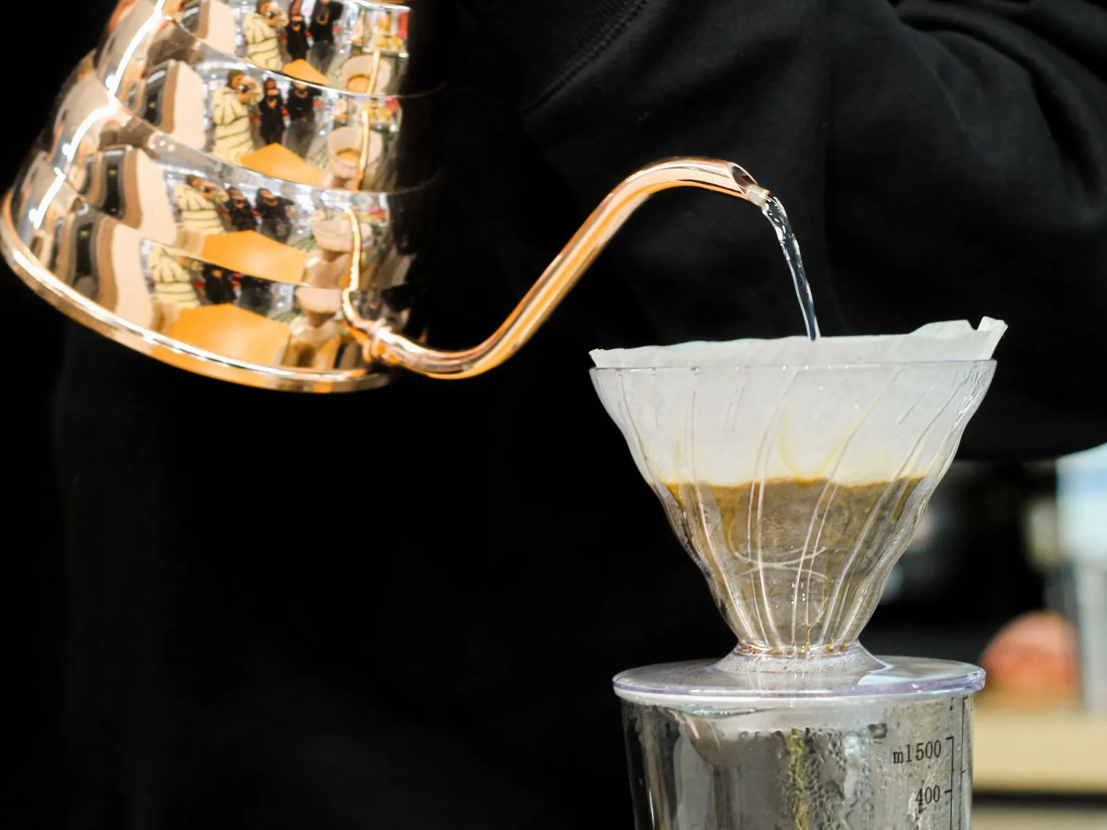 Barista pouring hot water from a copper gooseneck kettle over a paper filter dripper