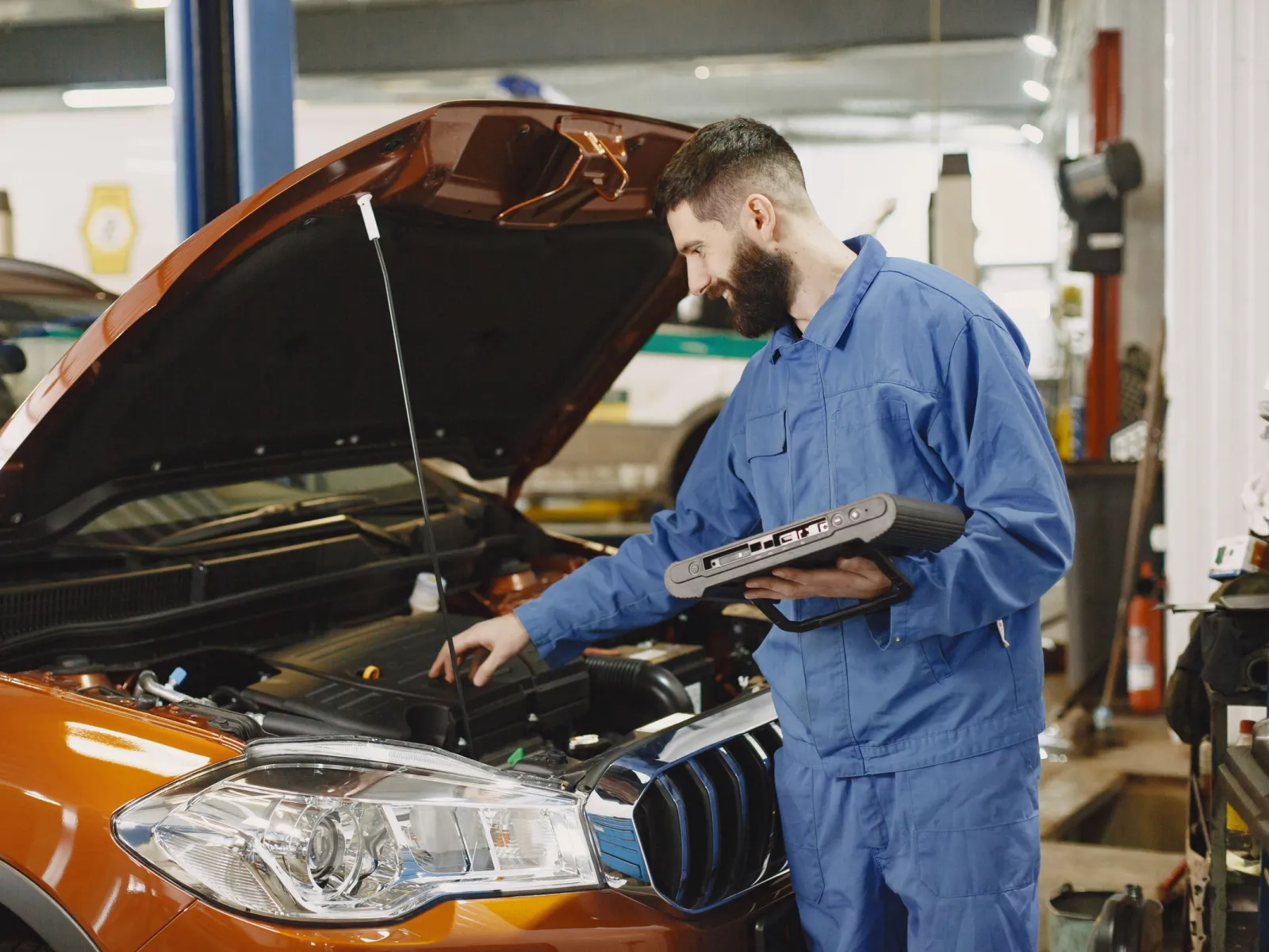 Mechanic holding a diagnostic scanner over the engine bay of an orange SUV