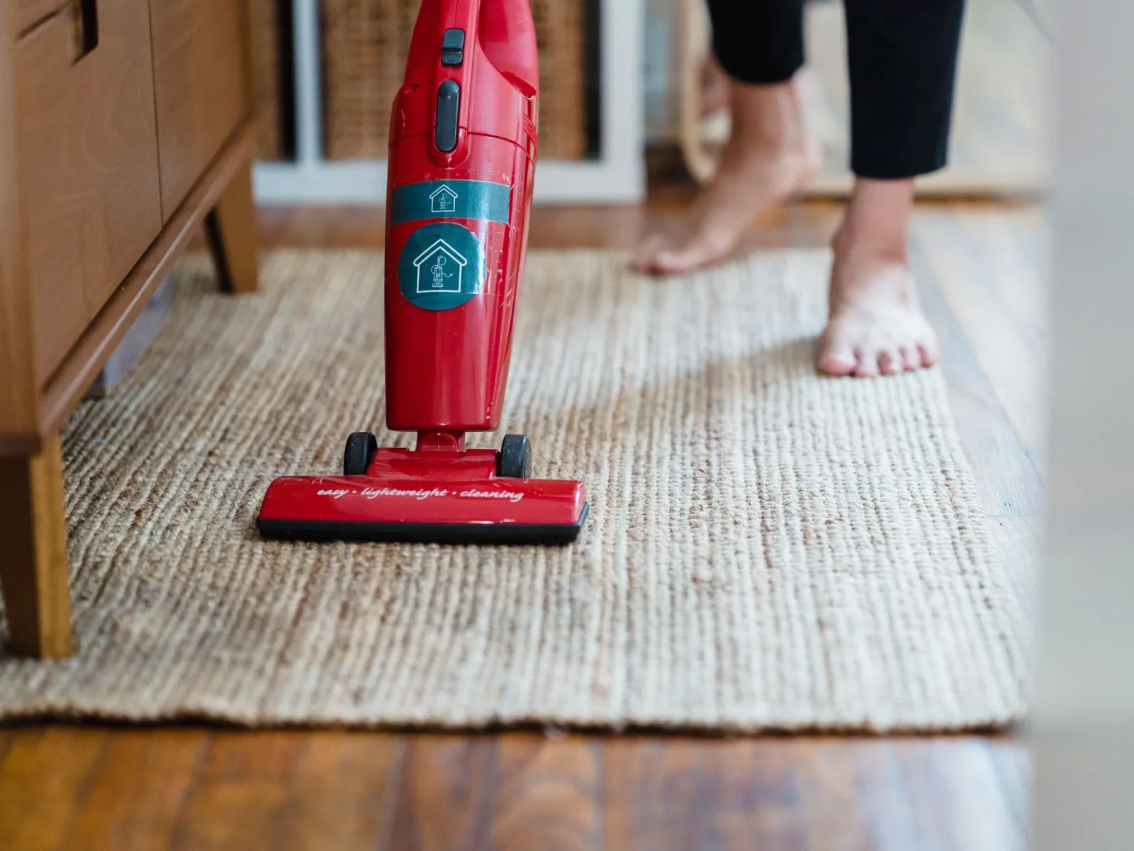 Red stick vacuum cleaning a woven jute rug in a bright living room