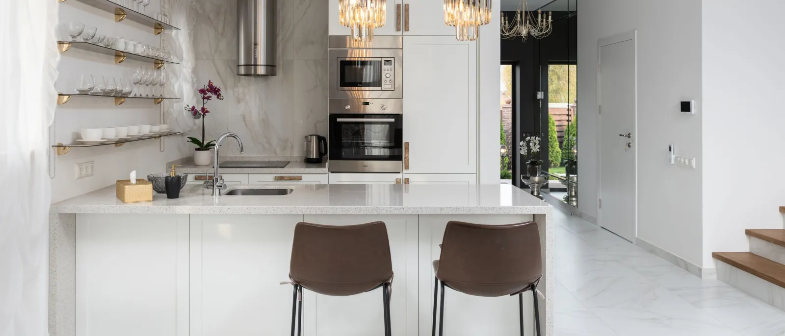 Gleaming white kitchen with marble backsplash and crystal pendant lights
