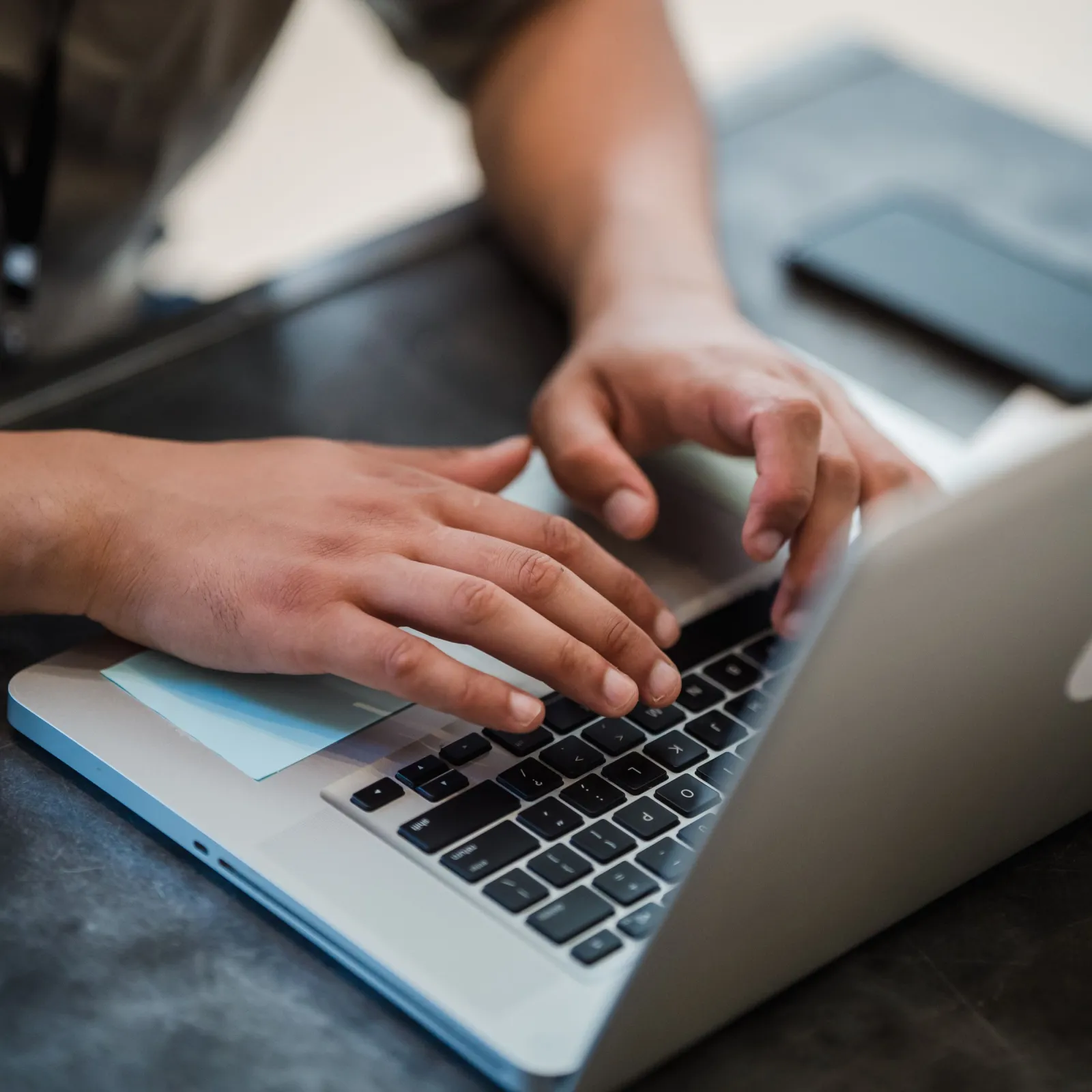 Close-up of hands typing on a silver laptop keyboard at a dark desk