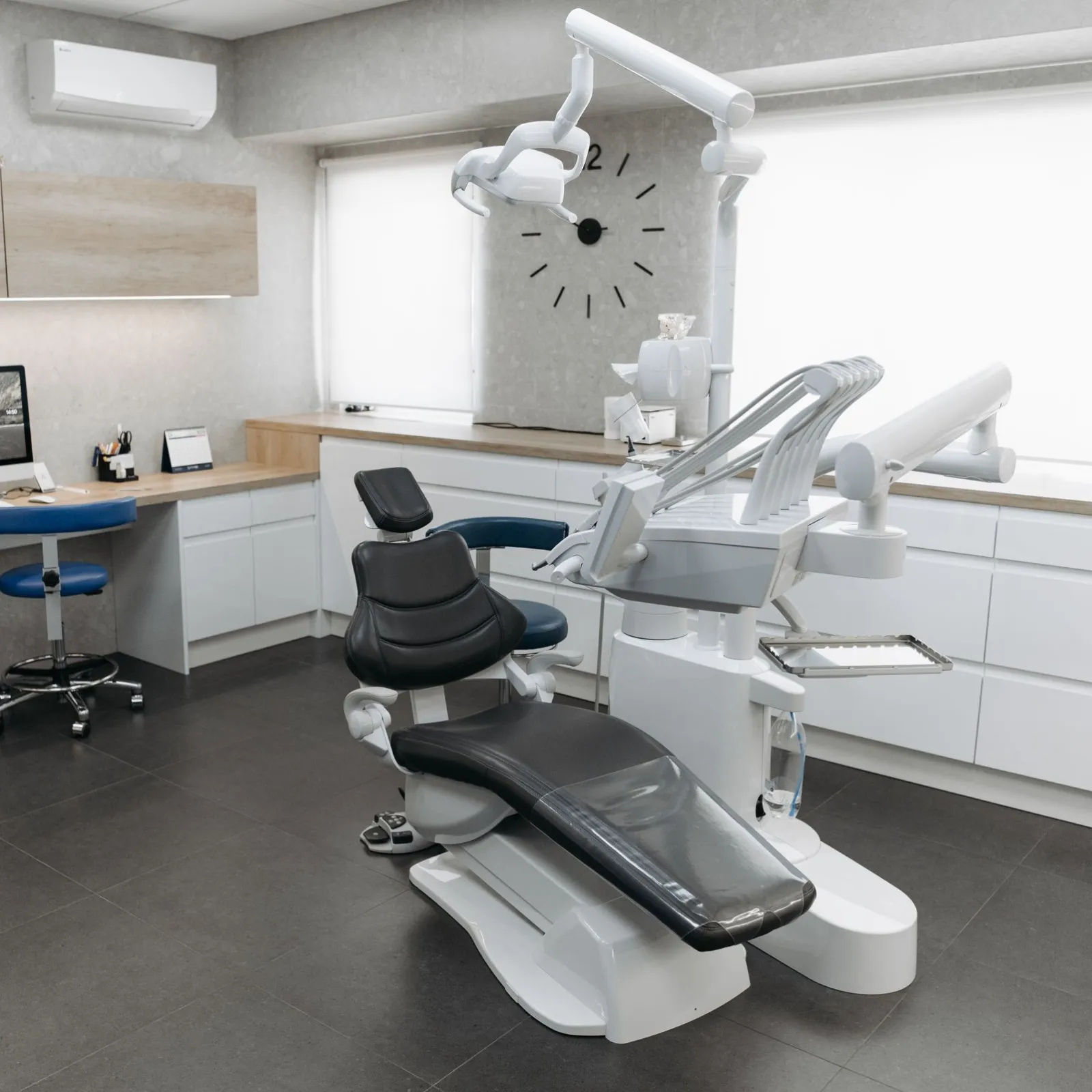 Modern dental treatment room with black chair, wood counters and a wall clock