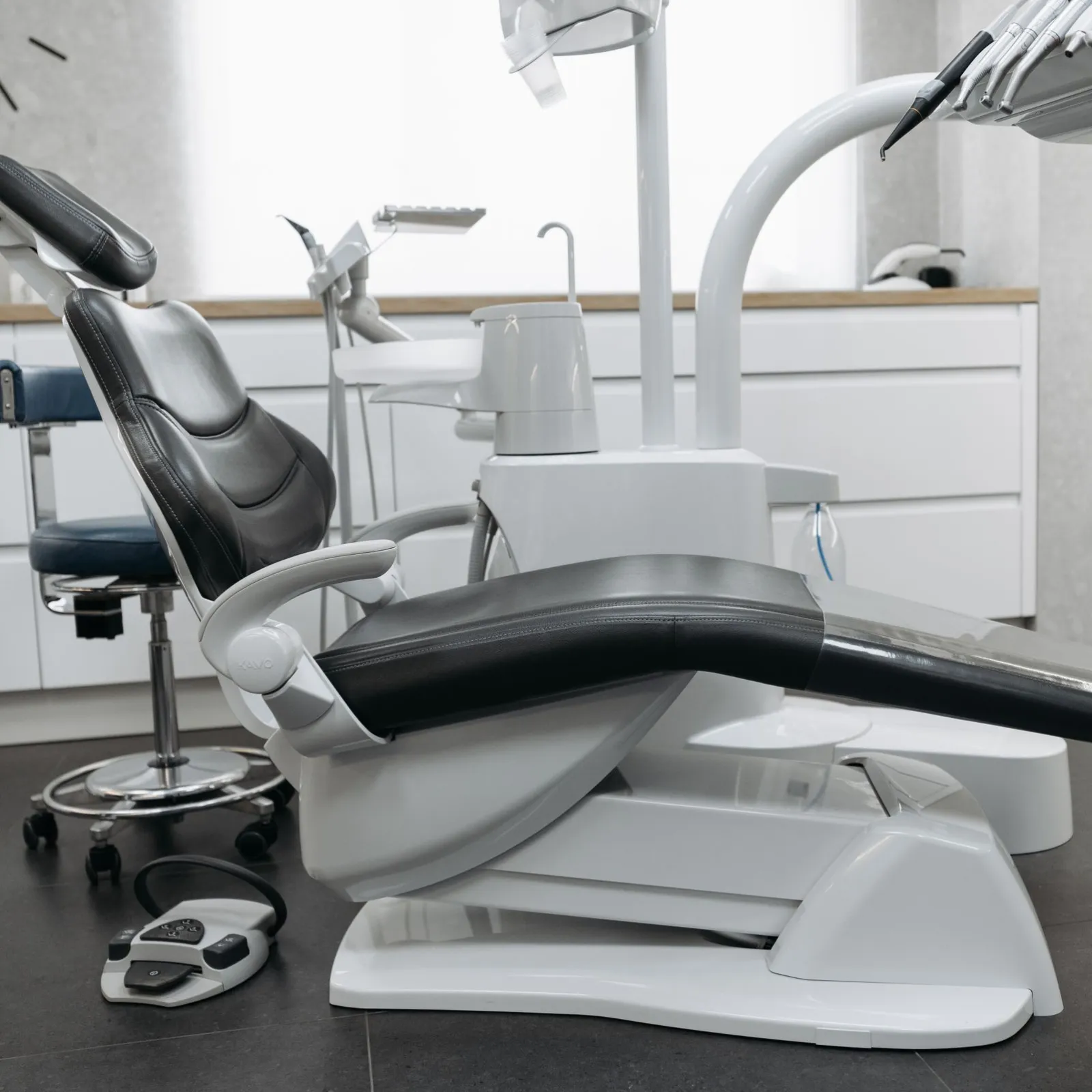 Side view of a reclined black dental chair with instrument arm in a gray and white clinic