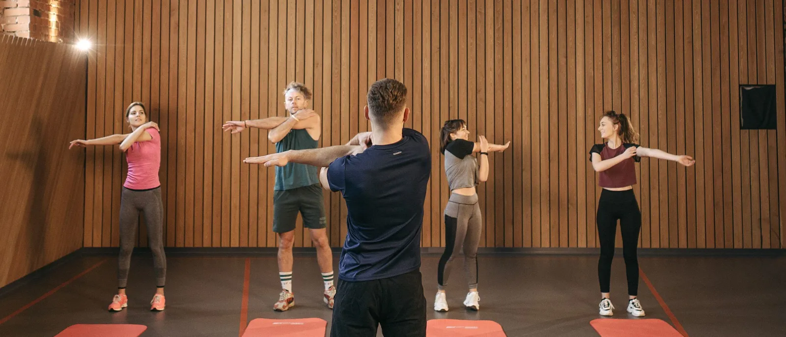 Instructor leading a small group fitness class stretching in a wood-panelled studio