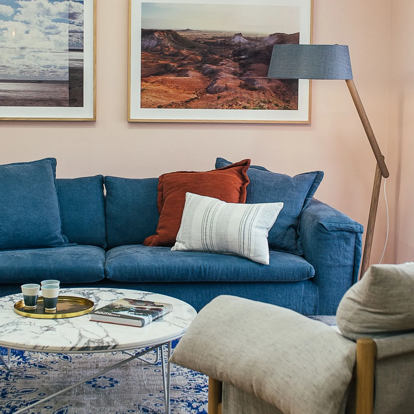 Blue velvet sofa with cushions against a blush pink wall hung with framed landscape prints