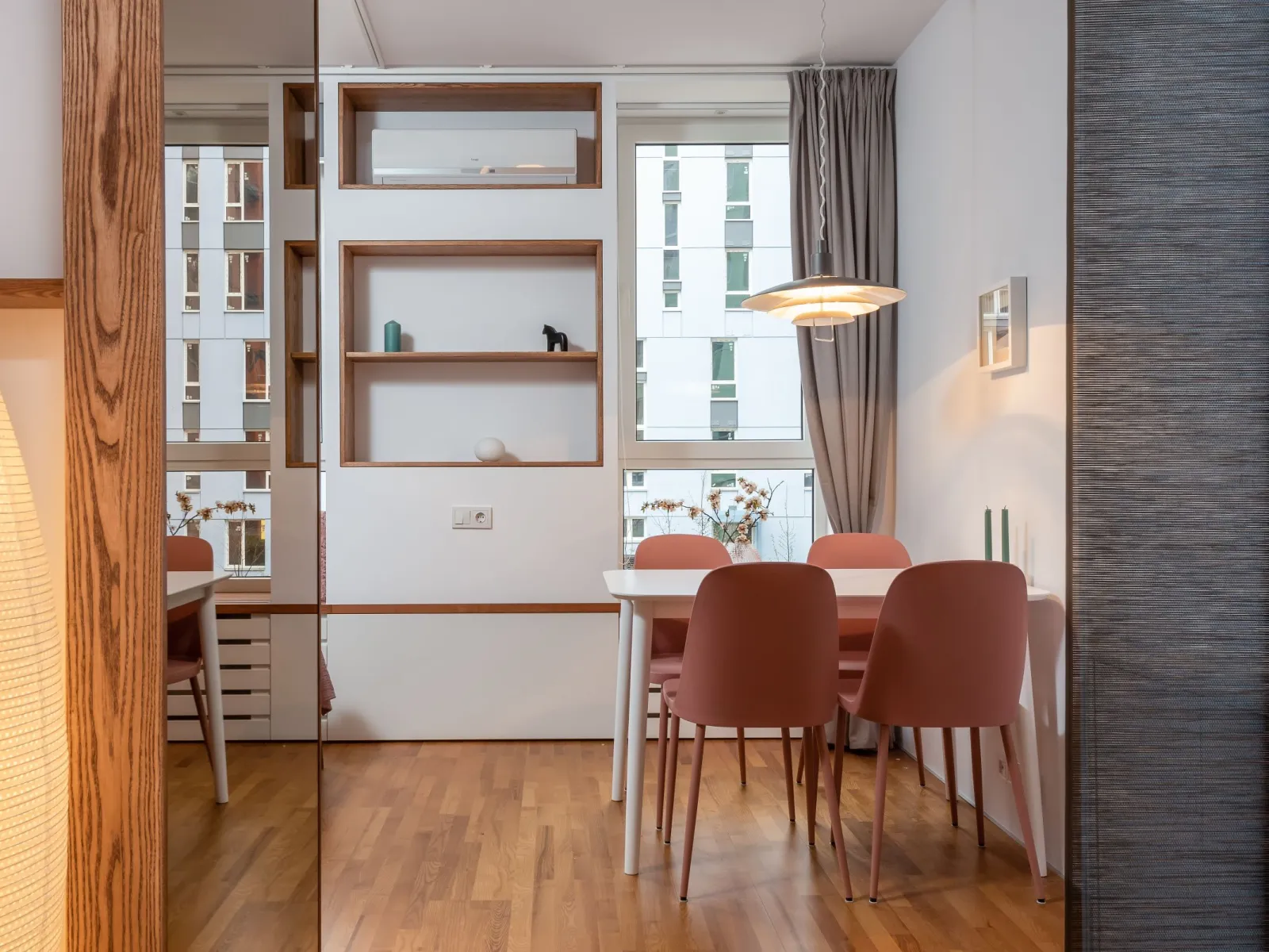 Dining nook with white table, dusty-pink chairs, pendant lamp and warm wood floor