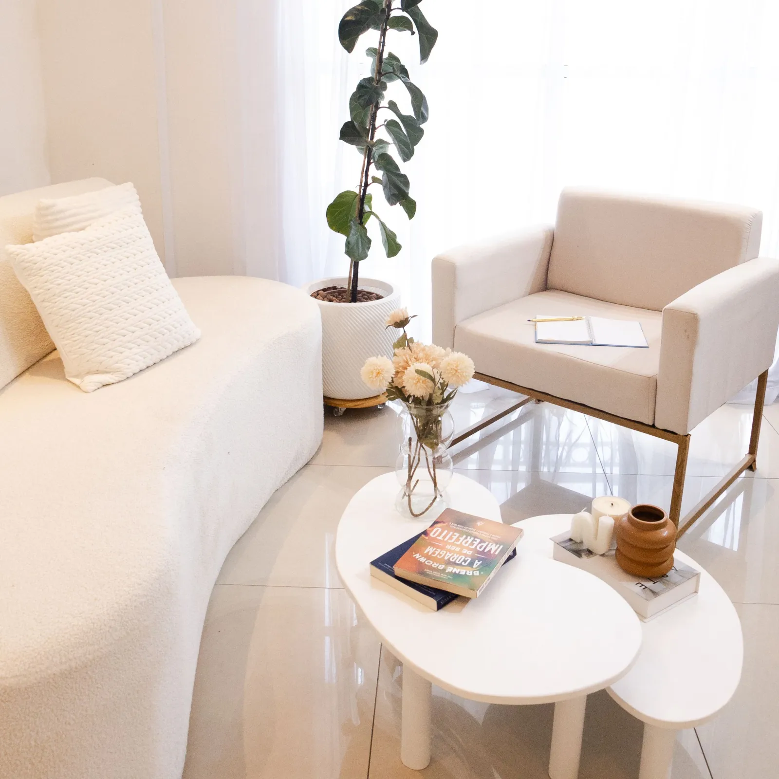 Bright white living room with curved boucle sofa, armchair, nesting coffee tables and a potted fig plant