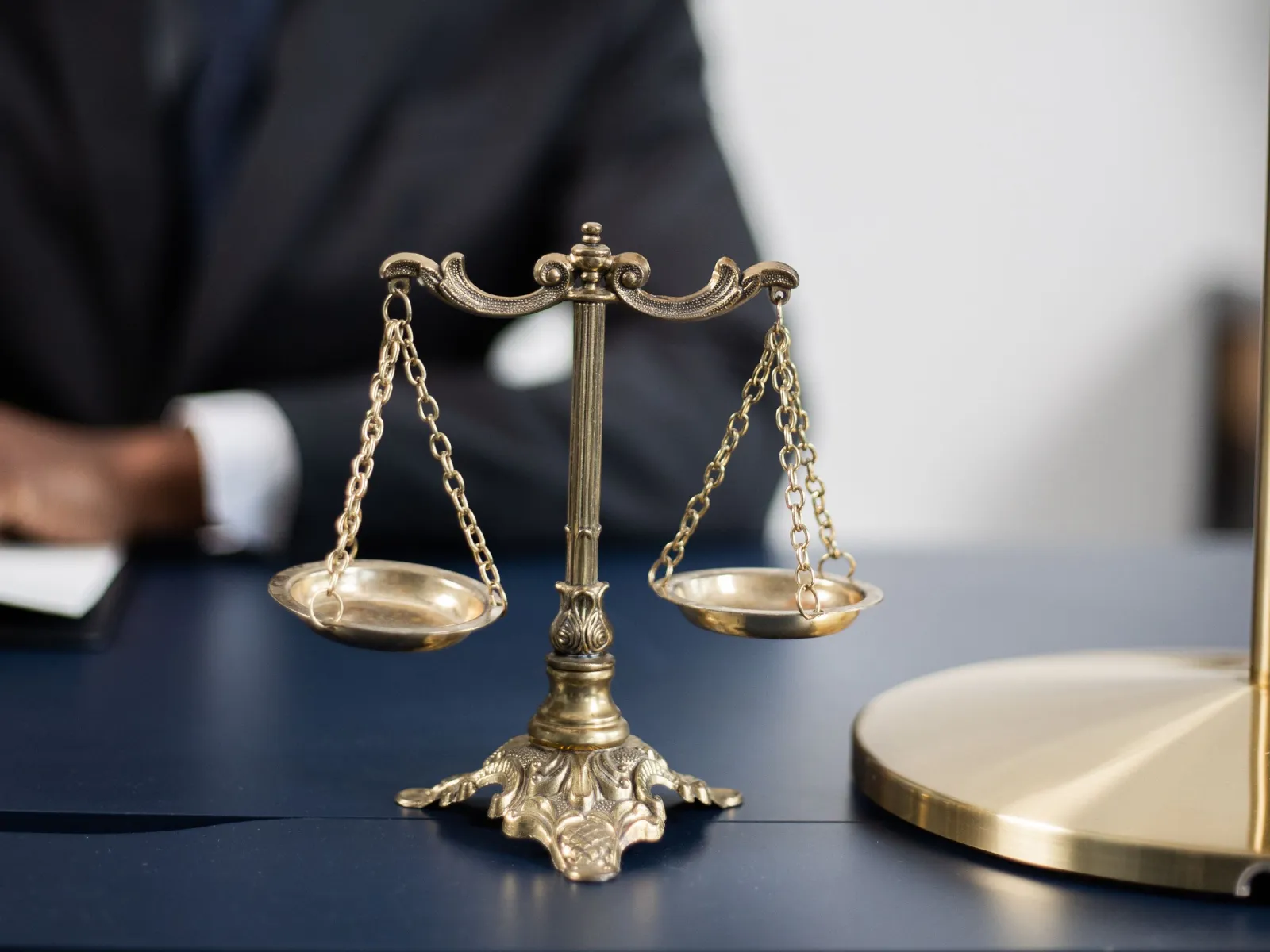 Brass balance scale on a navy desk with a lawyer working in the background