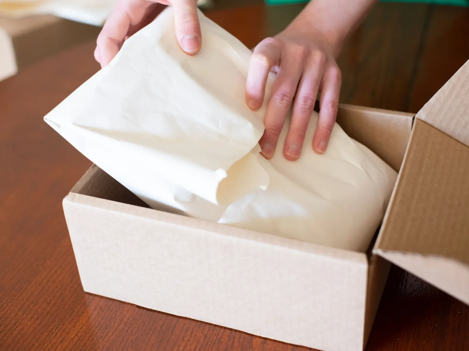 Close-up of hands wrapping an order in tissue paper inside a cardboard box
