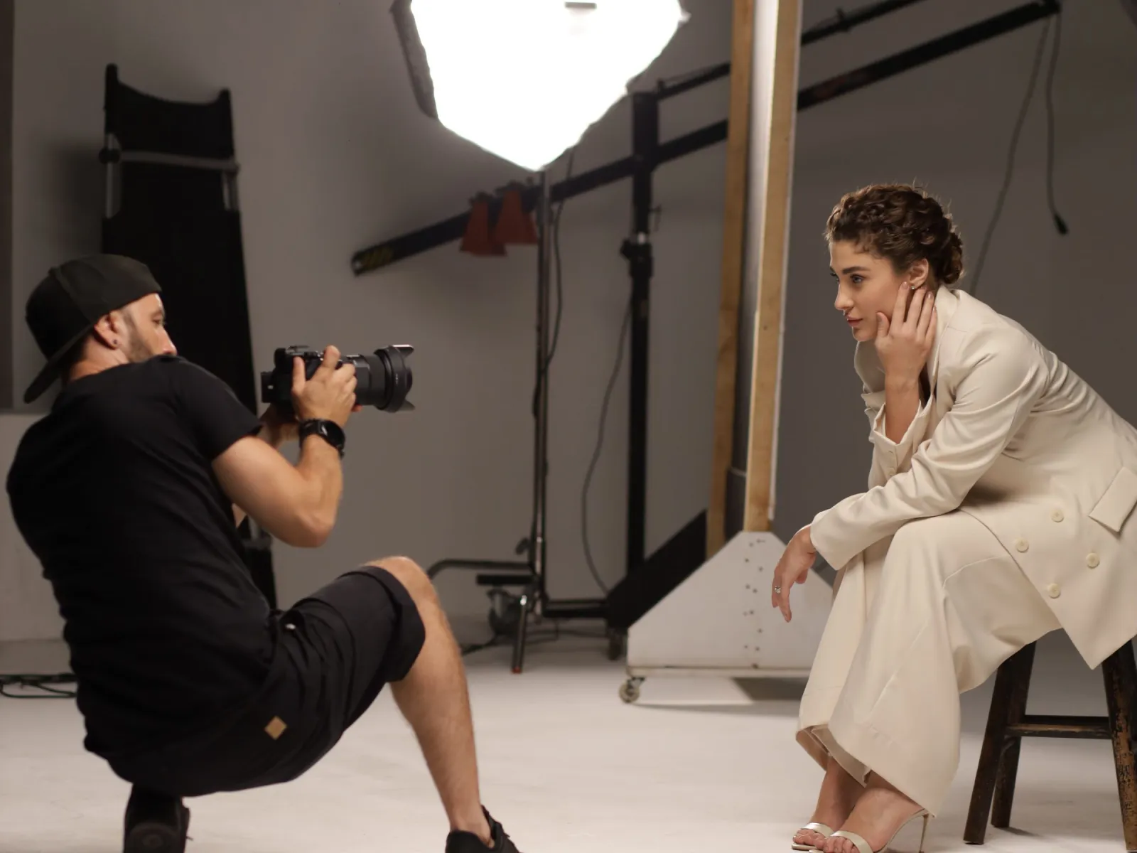 Photographer crouching to shoot a seated model under an octabox in a gray studio