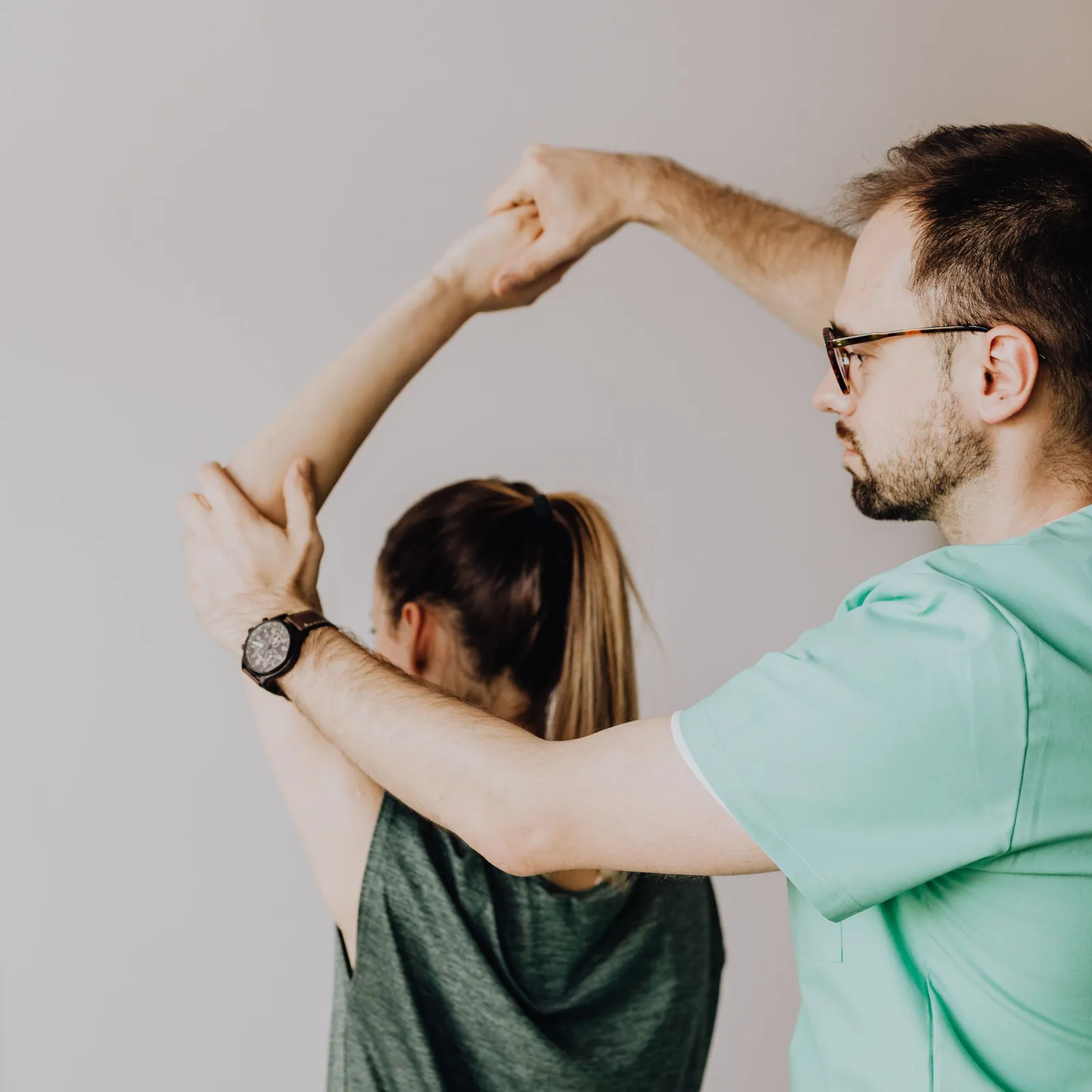 Physiotherapist raising the arm of a seated patient during a shoulder assessment in a white clinic