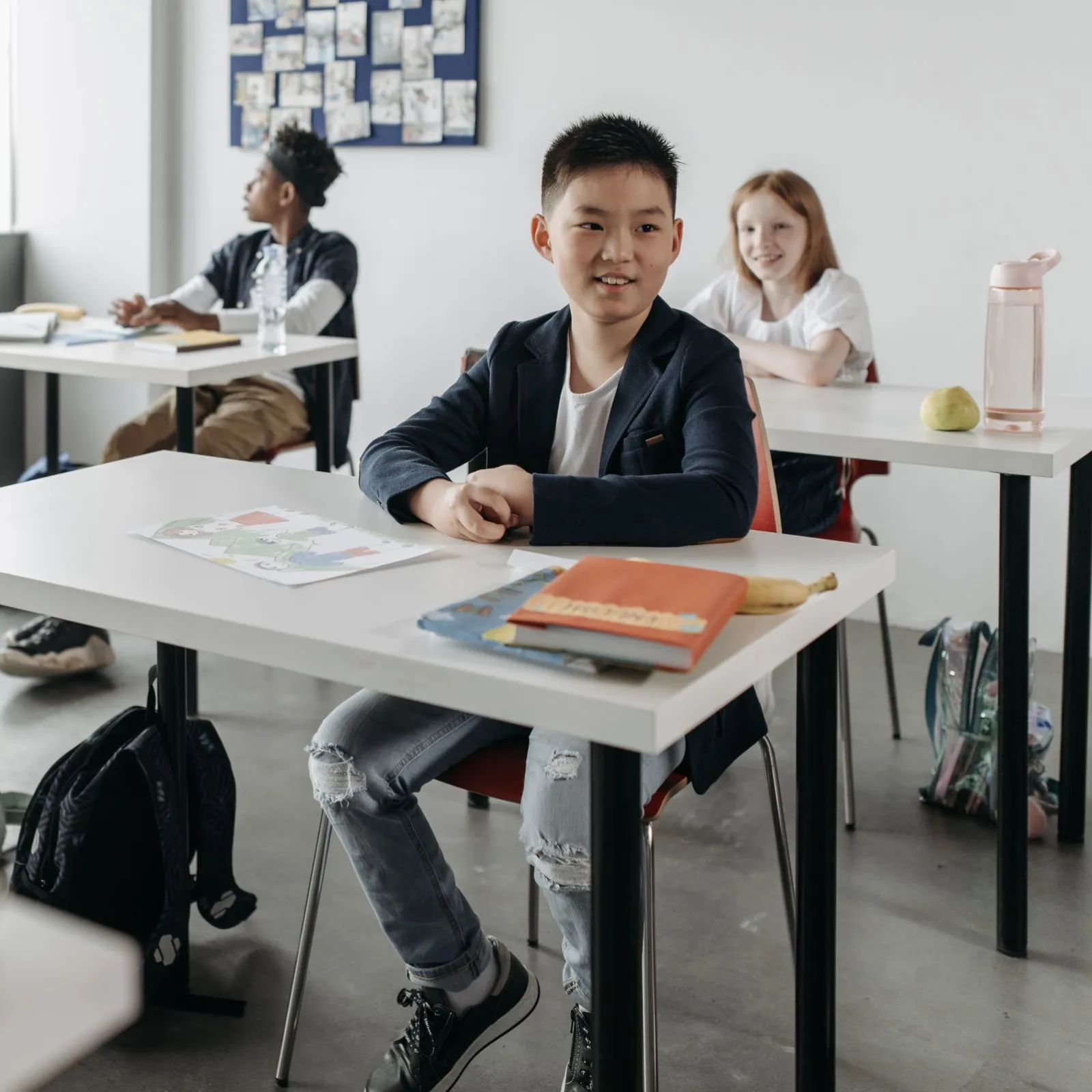 Four smiling students seated at white desks in a modern bright classroom