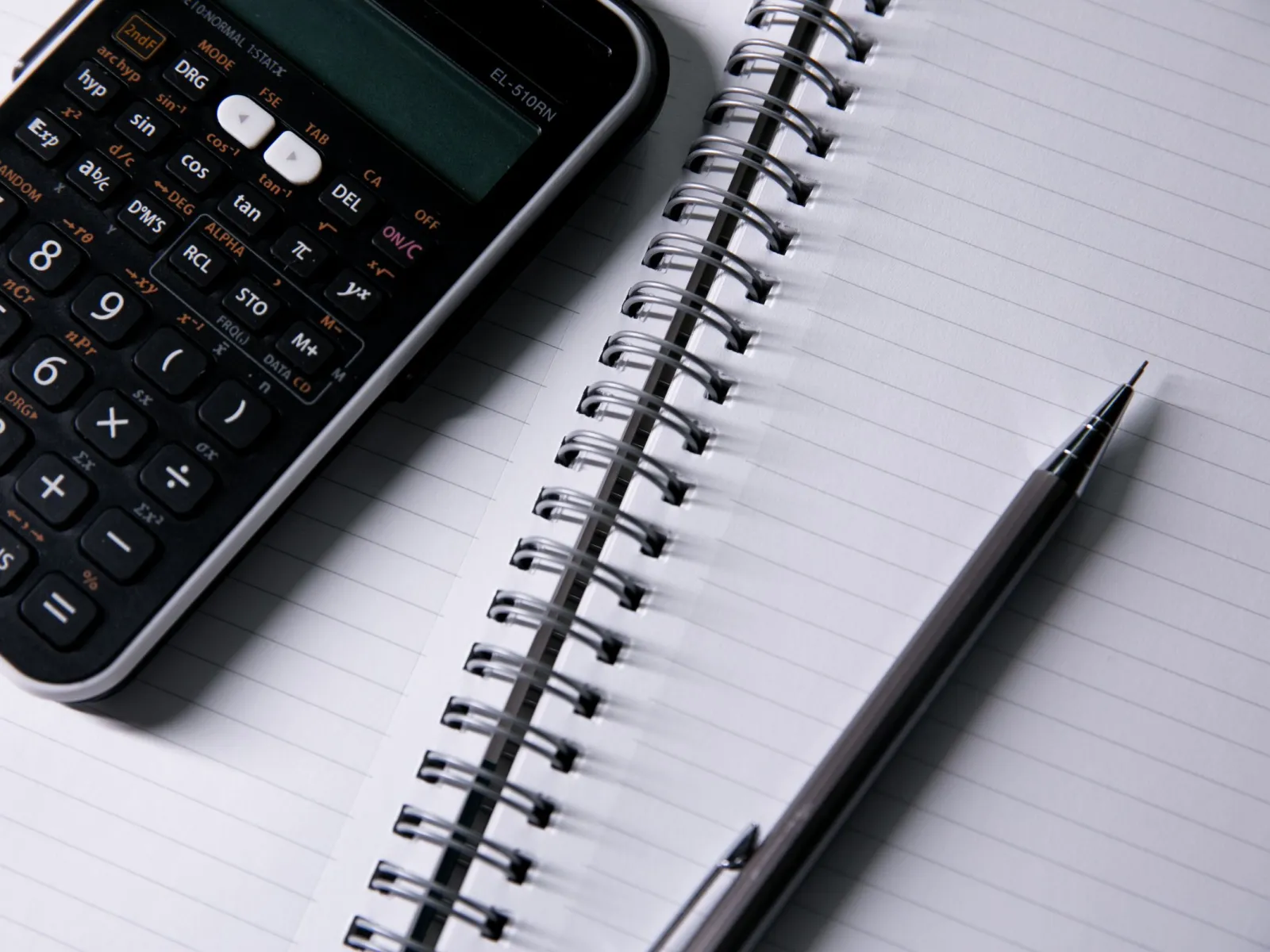 Close-up of a scientific calculator, spiral notebook and mechanical pencil
